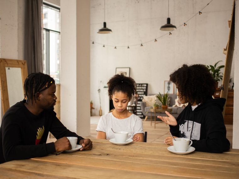 black parents lecturing upset daughter at table