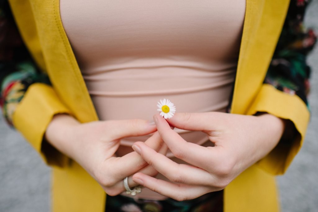 Woman wearing yellow holding a daisy.