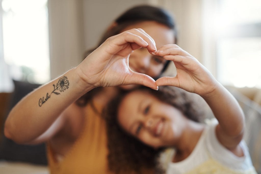 A parent and neurodivergent child joining hands to create a heart.