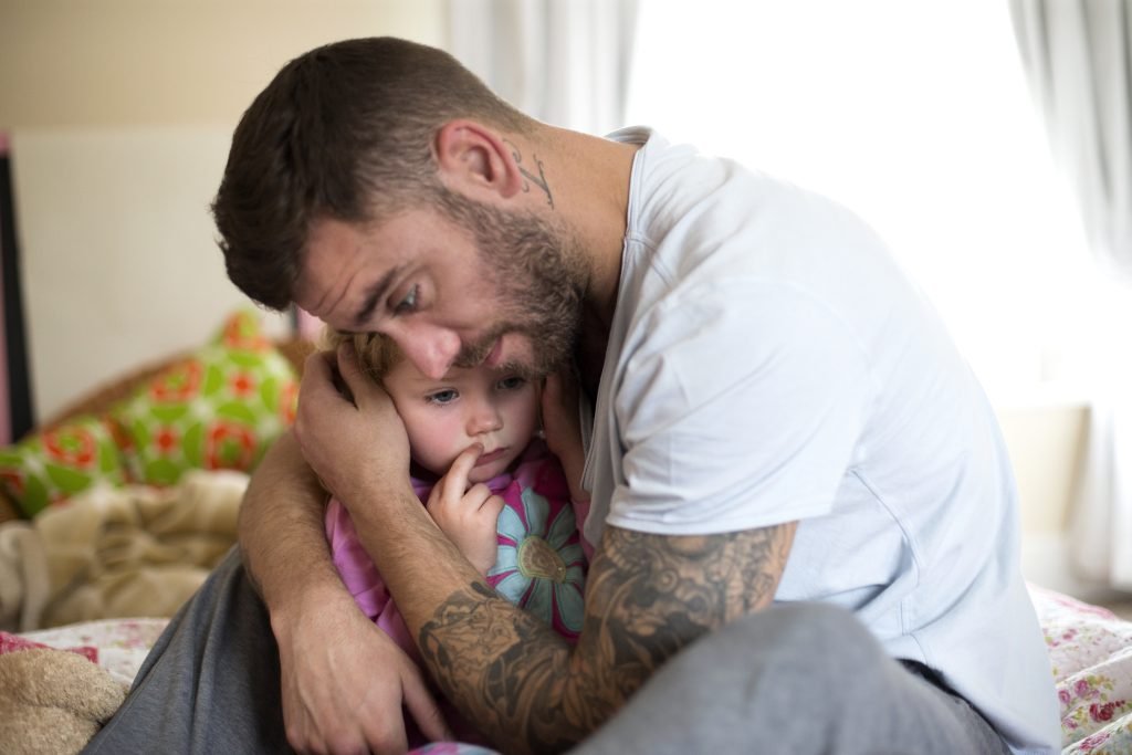 Father with a beard and tattoos comforting his toddler daughter