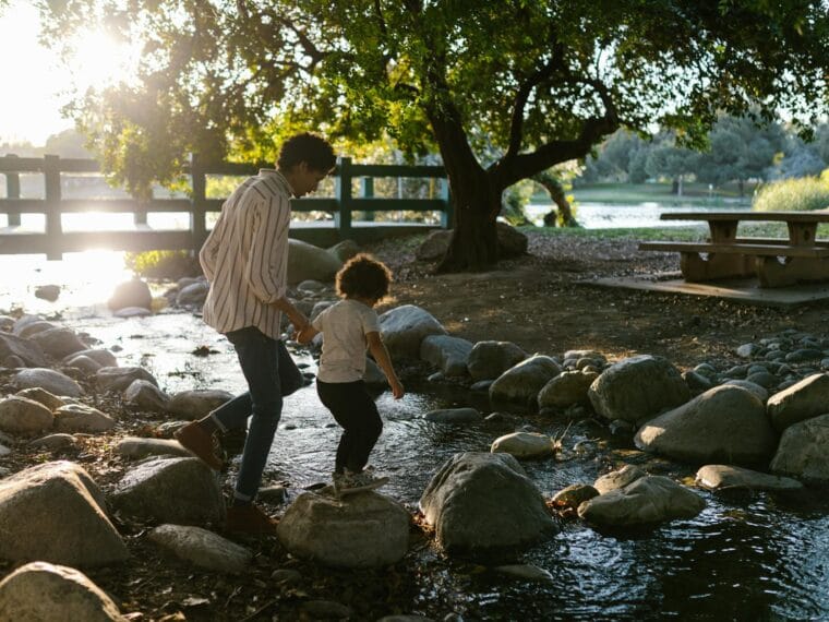 father and child walking on the rocky river
