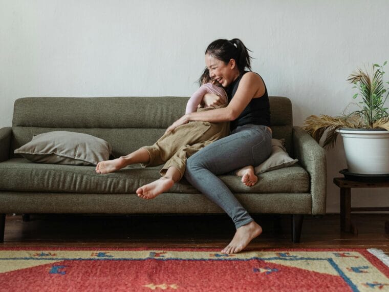 photo of woman sitting on couch while hugging her child