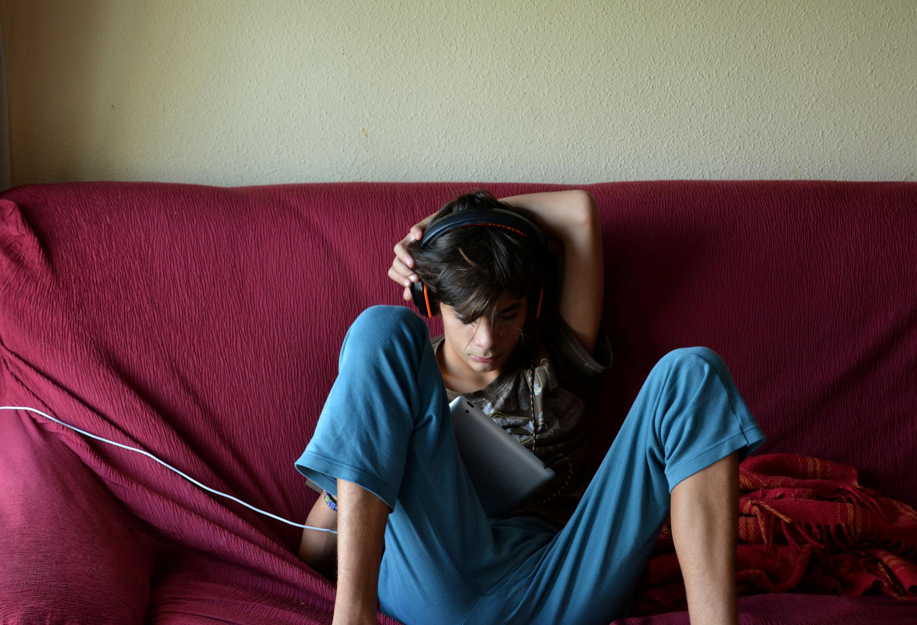 boy wearing headset while using ipad sitting on couch